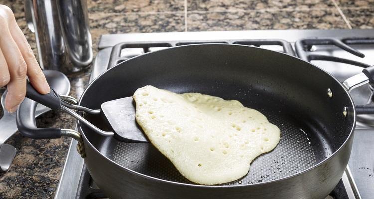 Horizontal photo of focus on pancake batter being fried into a pancake within hot frying pan