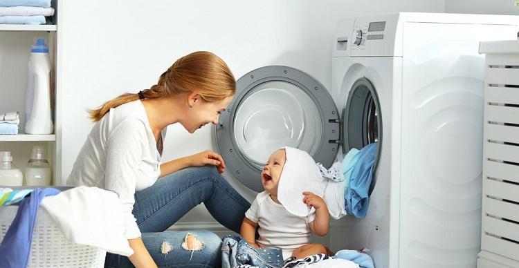 mother a housewife with a baby engaged in laundry fold clothes into the washing machine