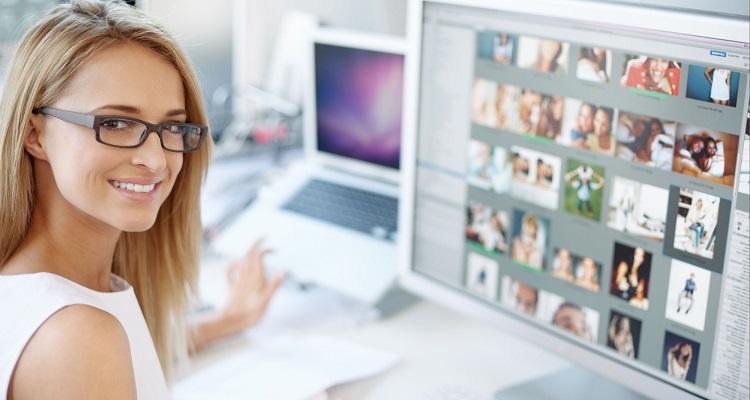 Portrait of young female designer sitting in office  with computer screen on front of her with images on