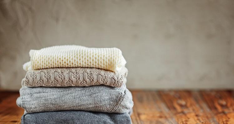 Stack of knitted winter clothes on wooden background, sweaters, space